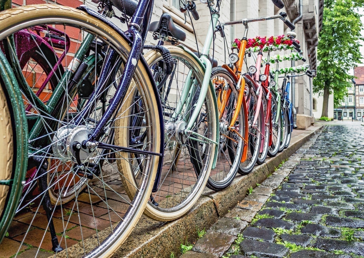 A colourful row of bicycles leaning against a building on a wet cobblestone street